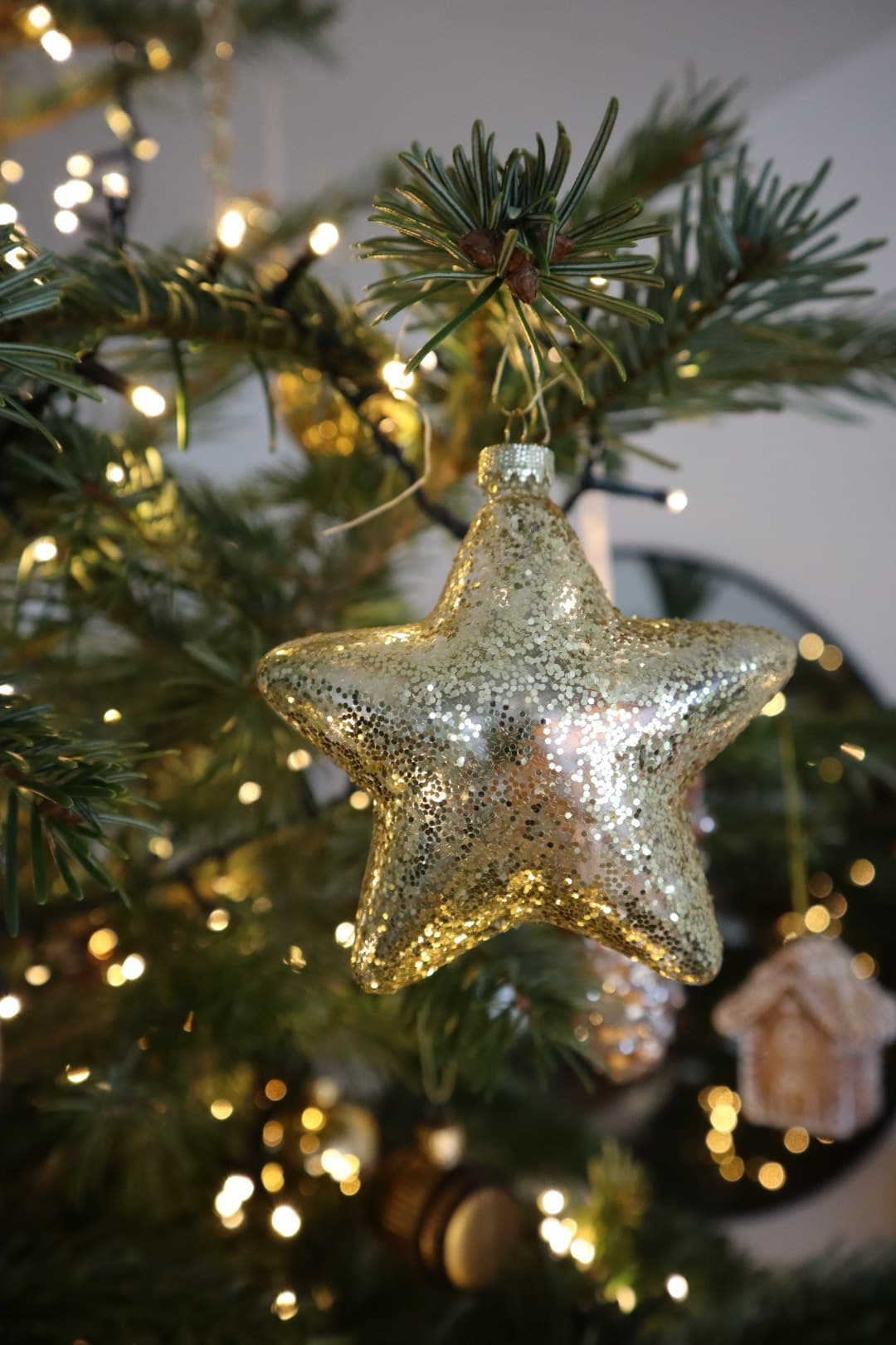 A gold star Christmas ornament hanging on a lit tree, with warm bokeh lights in the background.