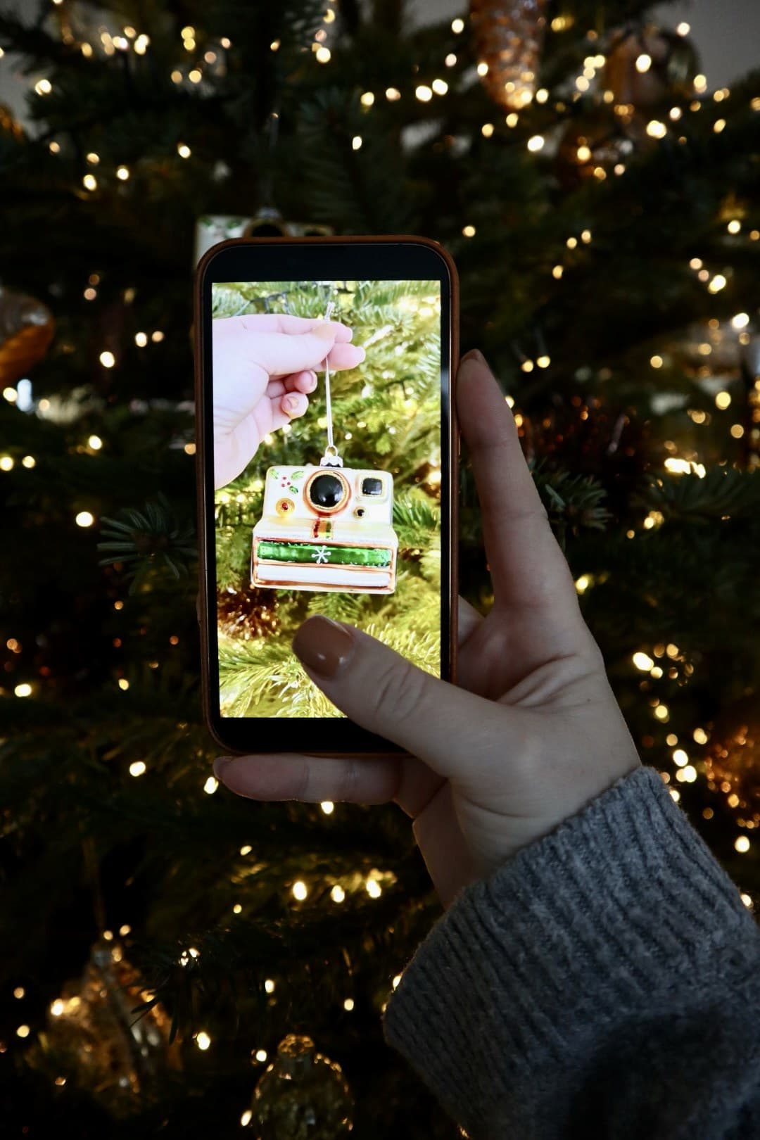 A small camera-shaped Christmas ornament with a Polaroid-style photo detail, hanging among fairy lights.
