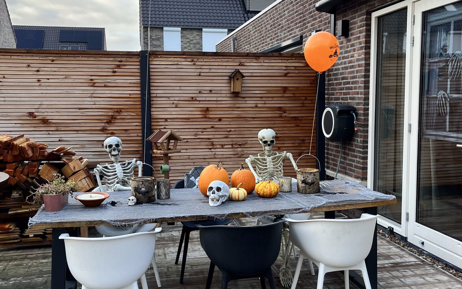 A long outdoor table set for the Halloween party, with seated skeletons, pumpkins and string lights.