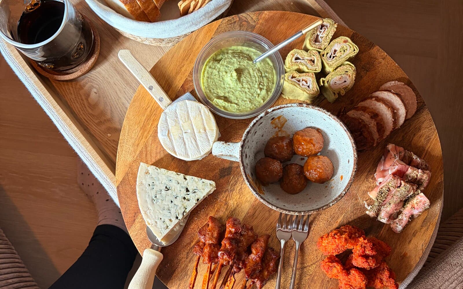 A large wooden board of picky bits - bread, cheese, a green dip, wraps, meatballs, warm bites and skewers, set out for the evening.