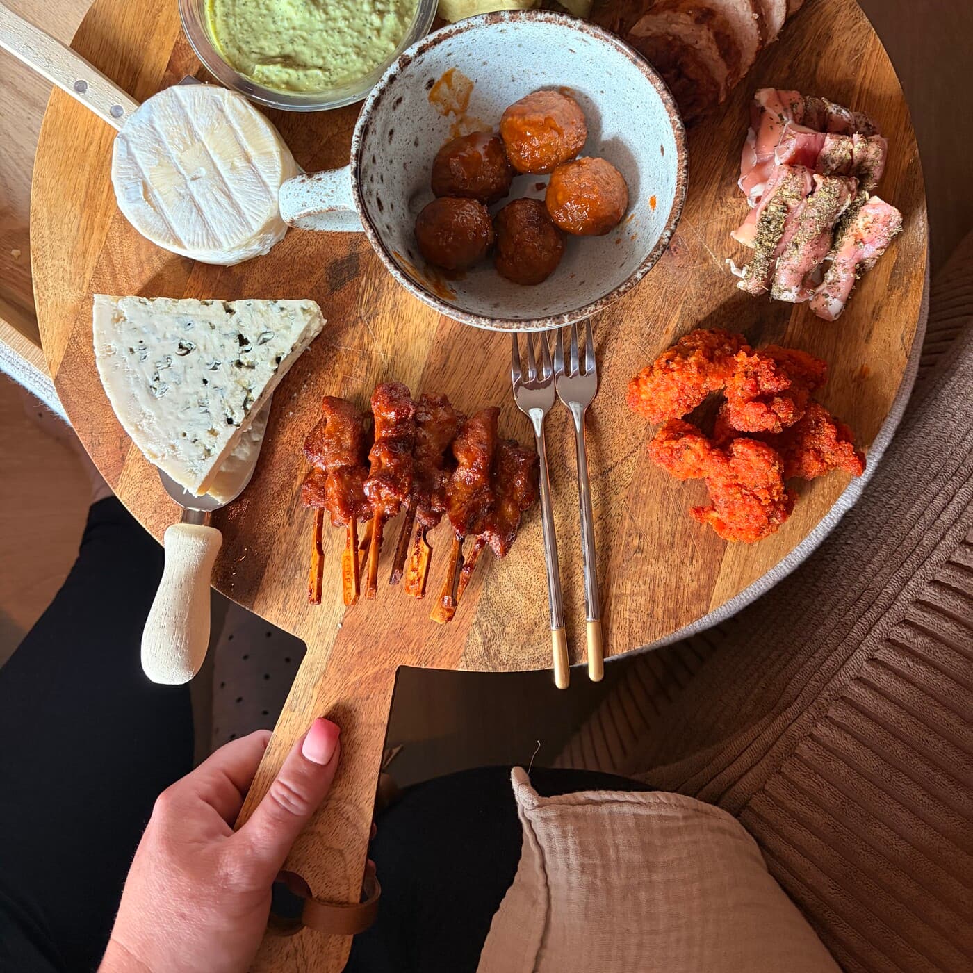 Esther holding the large round wooden picky-bits board, set with bread, cheese, dips and small plates.