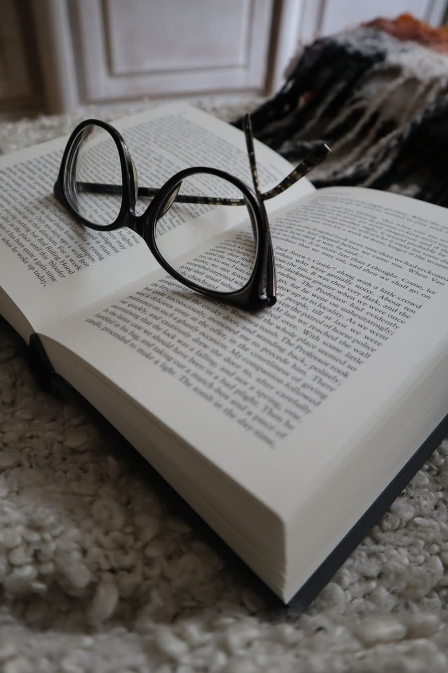 Reading glasses resting on the open pages of a gothic novel, softly lit in a quiet room.