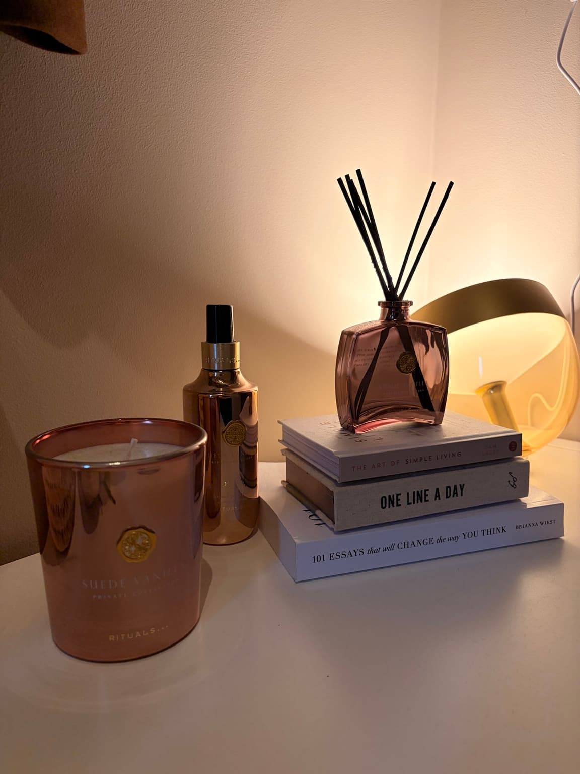 Rituals Suede Vanilla candle, room spray and reed diffuser styled with books and a warm table lamp.