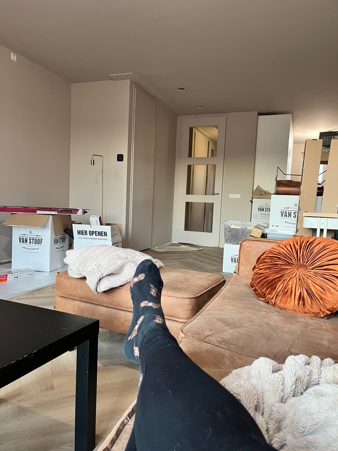 Old brown sofa used temporarily in a new home with boxes still visible.