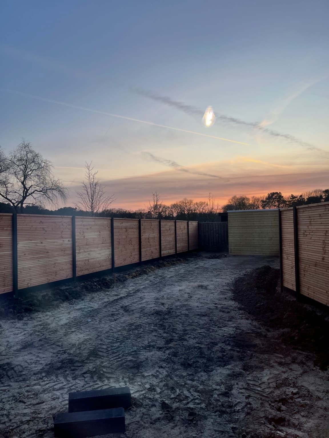 Bare unfinished garden behind a new-build home at sunset.