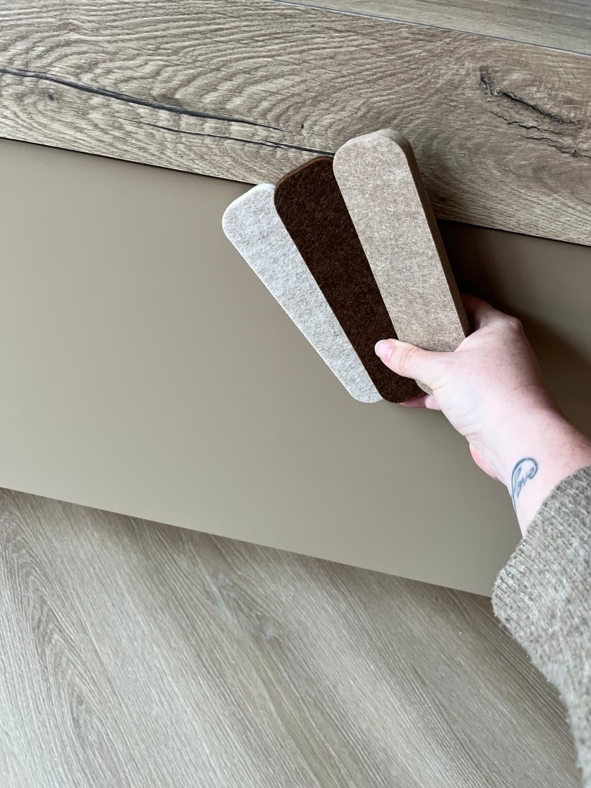 Hand holding warm material and colour samples against taupe cabinetry and a wood surface.