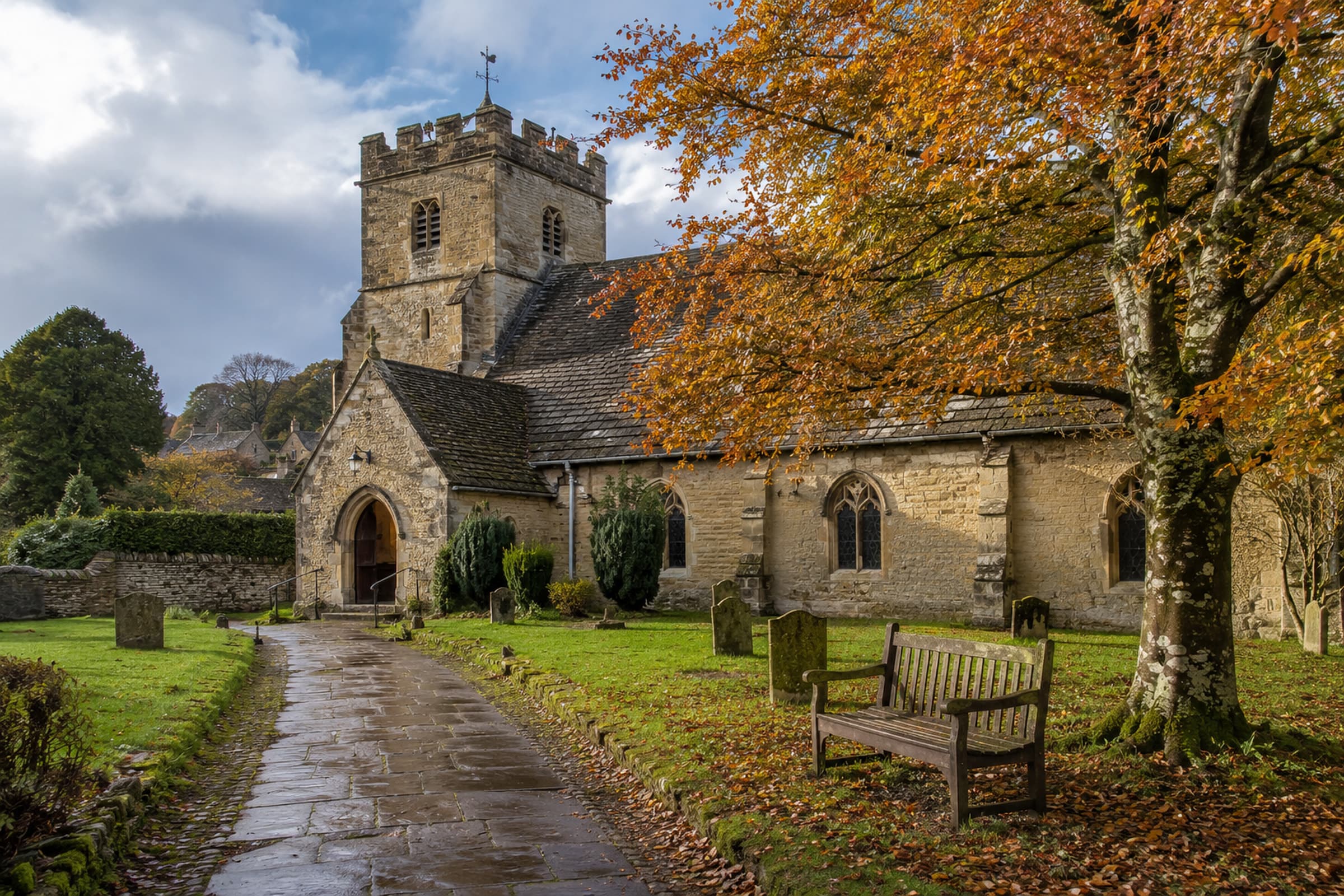 St Anne’s low stone tower and rain-darkened path beneath a mature beech tree.