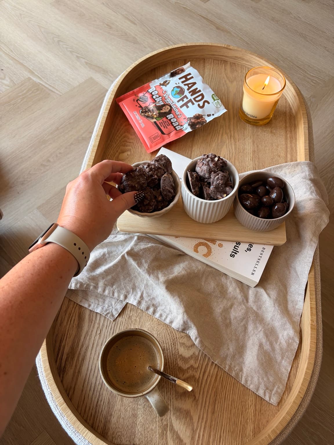 A hand reaching for a piece of Rocky Road chocolate bite from a small bowl on a wooden tray.