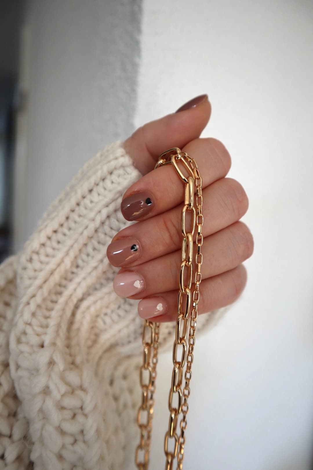 Hand holding layered gold necklaces against a soft cream knitted sleeve.