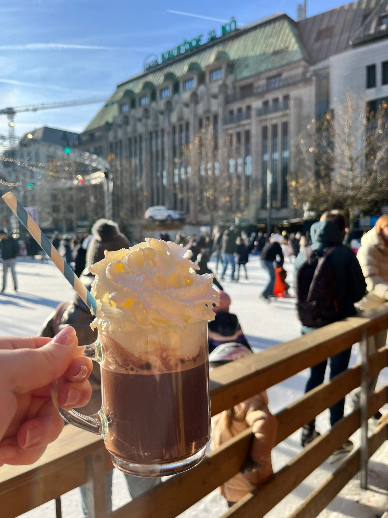 Hot chocolate with whipped cream held up at a sunny Christmas market