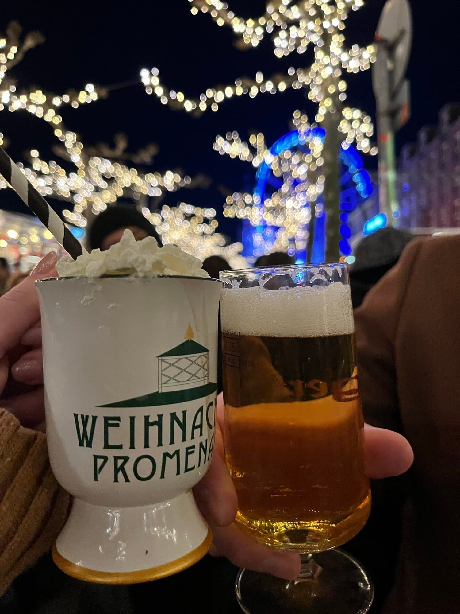 Two Weihnachtspromenade Glühwein mugs with Christmas-market lights in the background