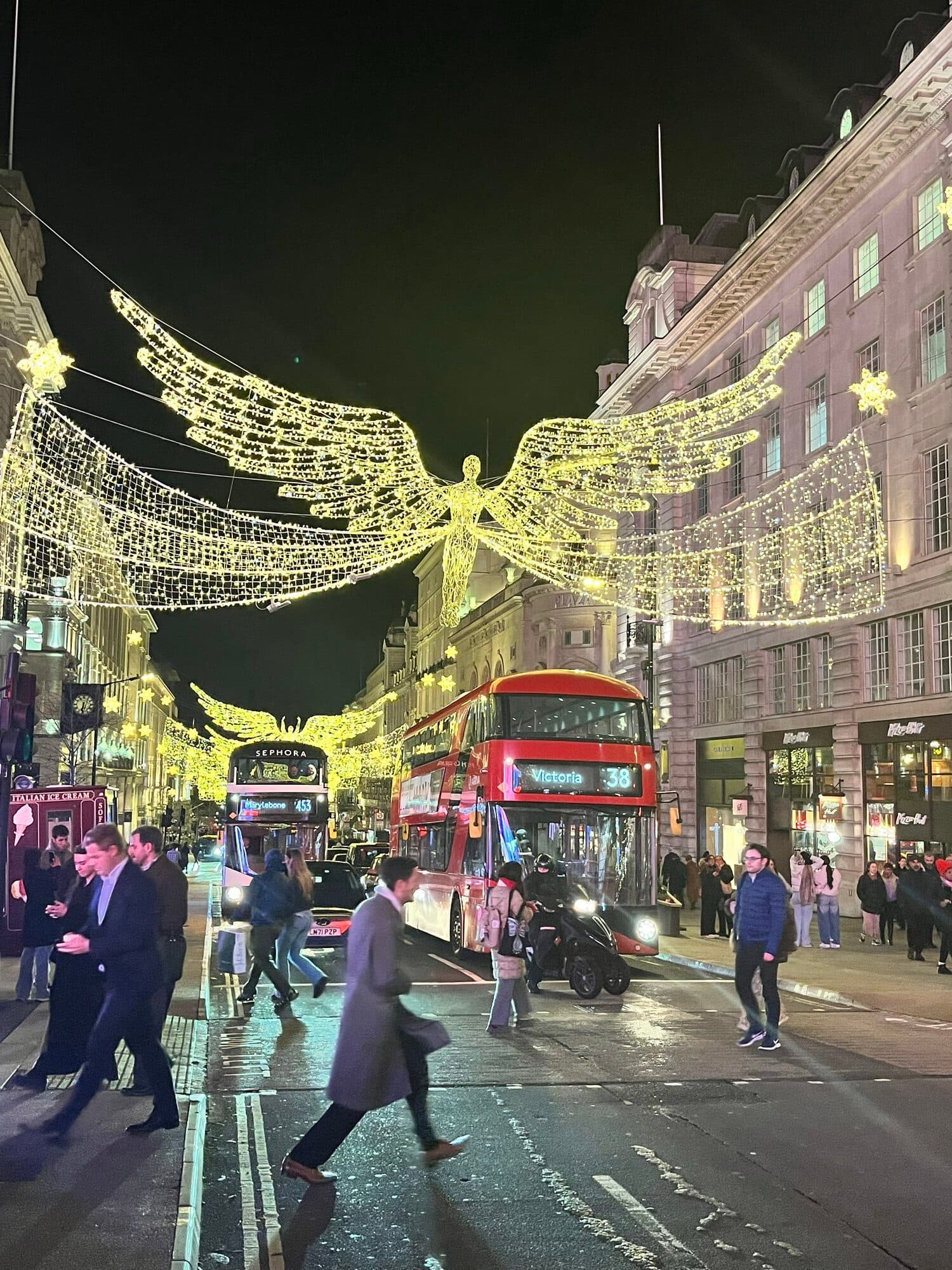 Illuminated Christmas lights above Regent Street in London, with a red bus passing below