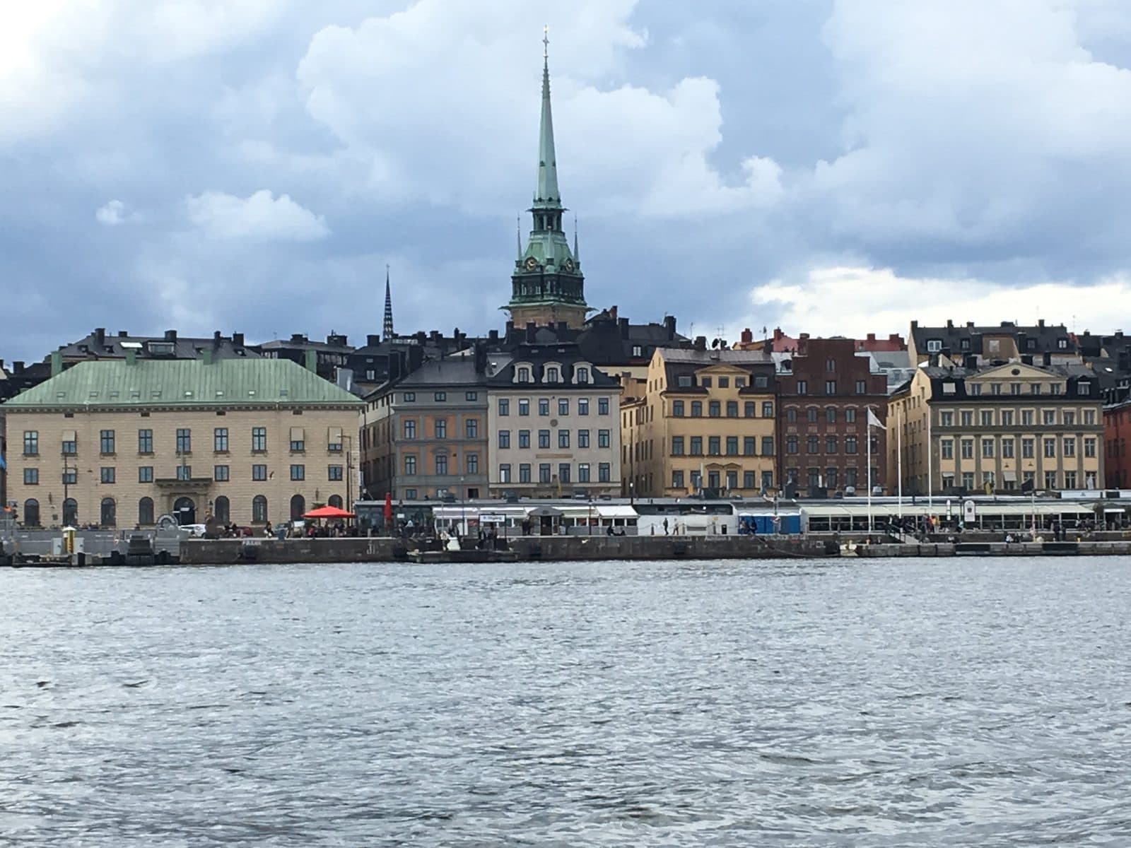 Gamla Stan’s waterfront with a green church spire and colourful old buildings across the water under scattered clouds