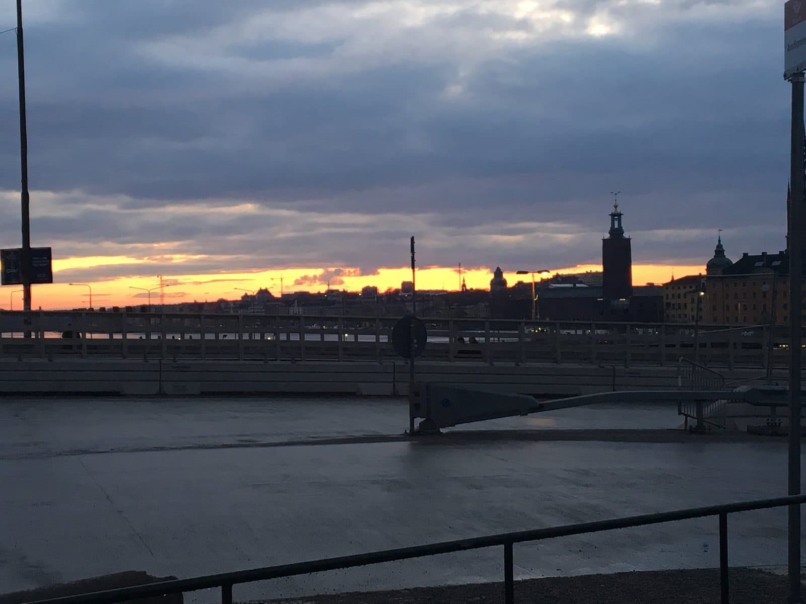 A strip of golden sunset light over the water and the Stockholm skyline, with City Hall’s tower in silhouette under dark clouds