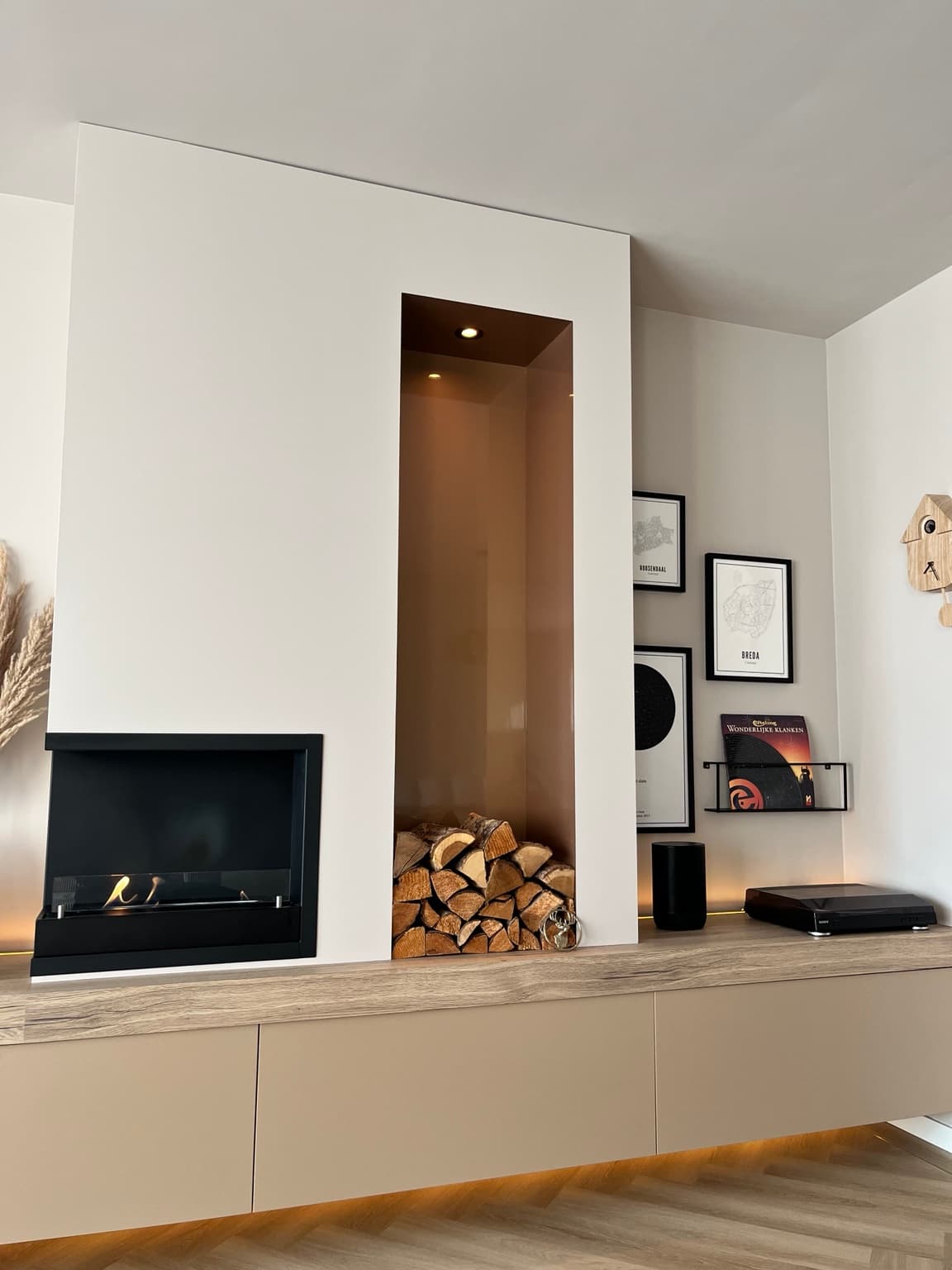 Warm finished living room with a built-in fireplace, log niche, artwork and softly lit cabinetry.