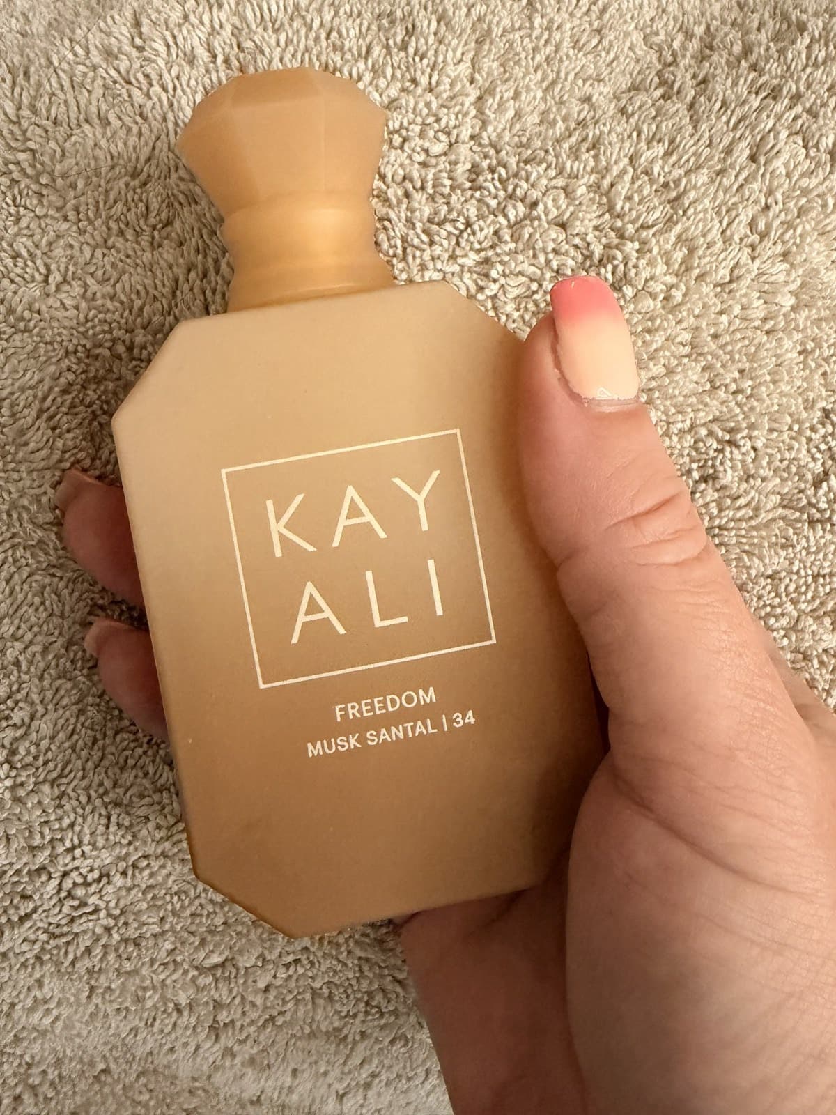 A bottle of Kayali Freedom Musk Santal | 34 eau de parfum held on a woven rug.