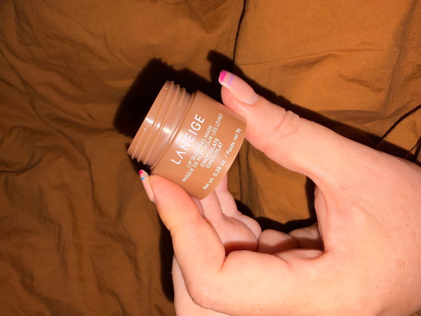 A jar of Laneige Lip Sleeping Mask in Chocolate held up close, its lid unscrewed.