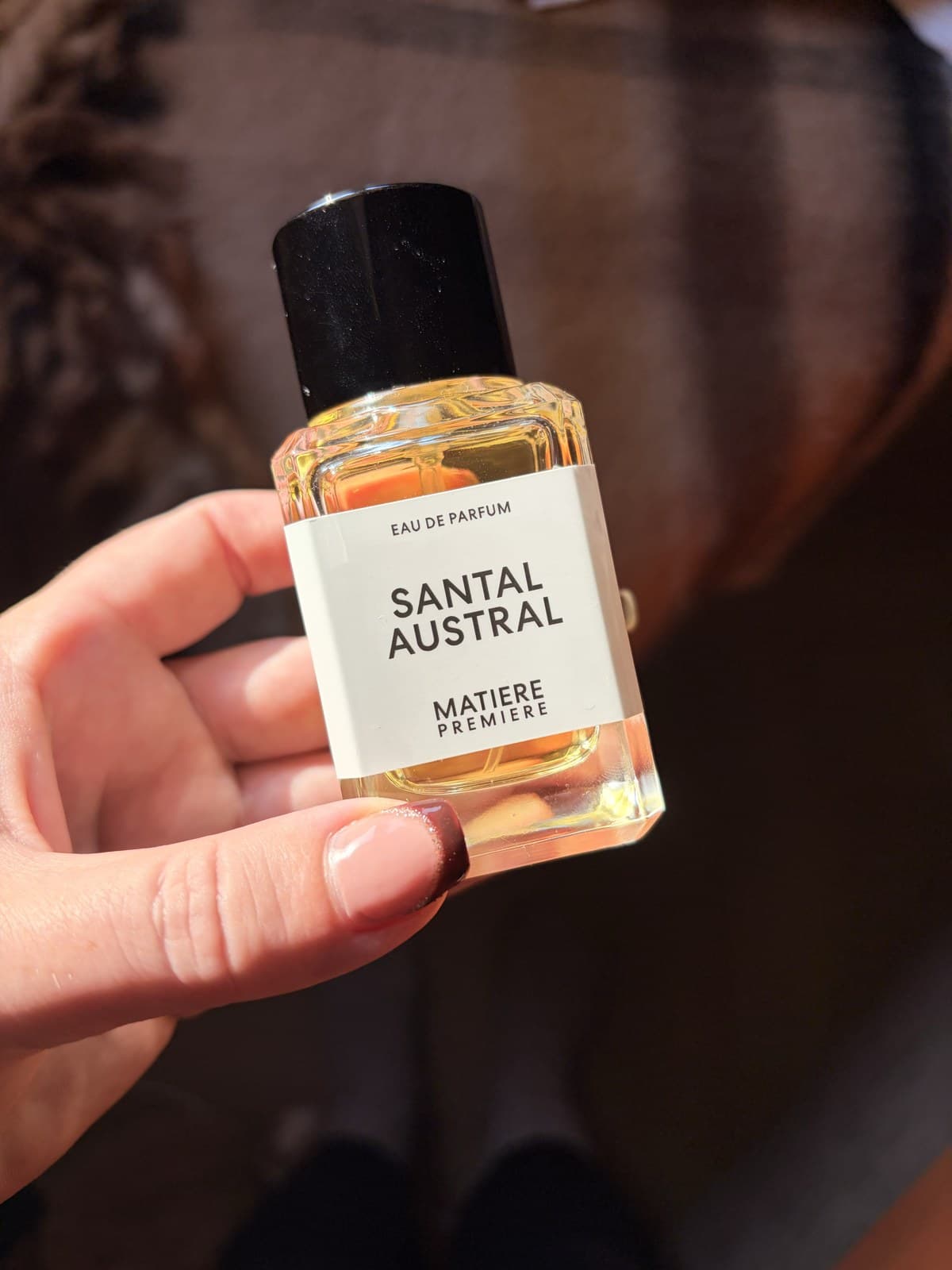 A bottle of Matiere Premiere Santal Austral eau de parfum held in one hand, its white label facing the camera.