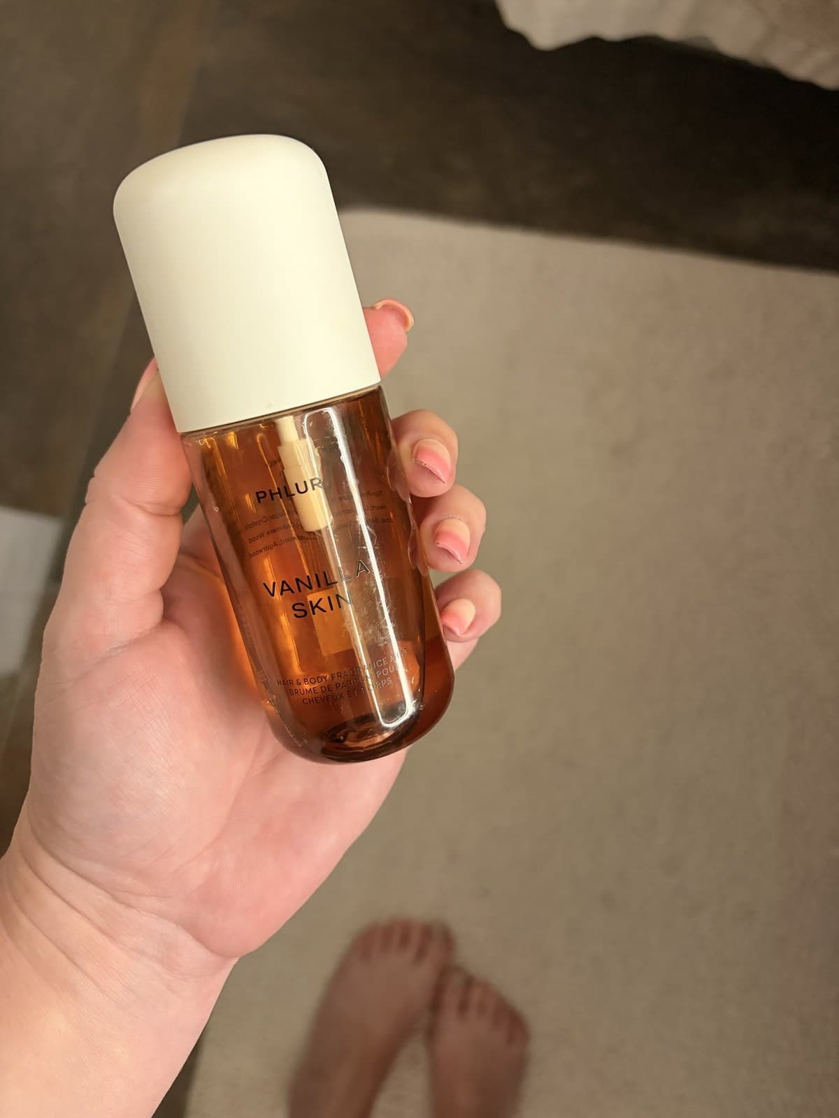A bottle of Phlur Vanilla Skin hair and body fragrance mist held in one hand.