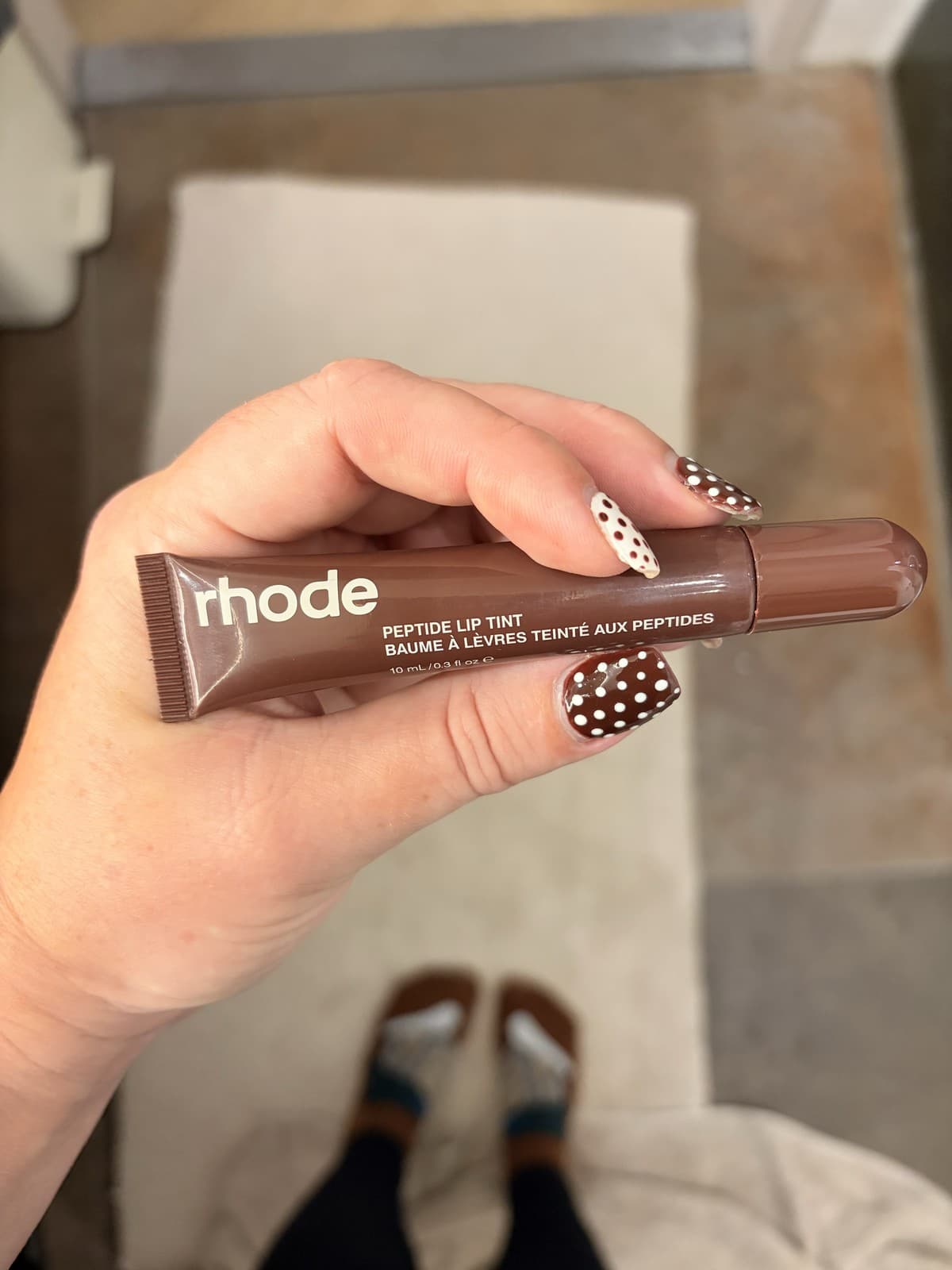 A tube of rhode Peptide Lip Tint held in one hand, its brown squeeze tube label facing the camera.