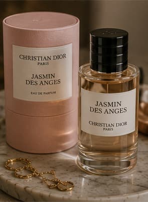 A boxed and unboxed bottle of Christian Dior Jasmin des Anges perfume beside gold jewellery on marble.