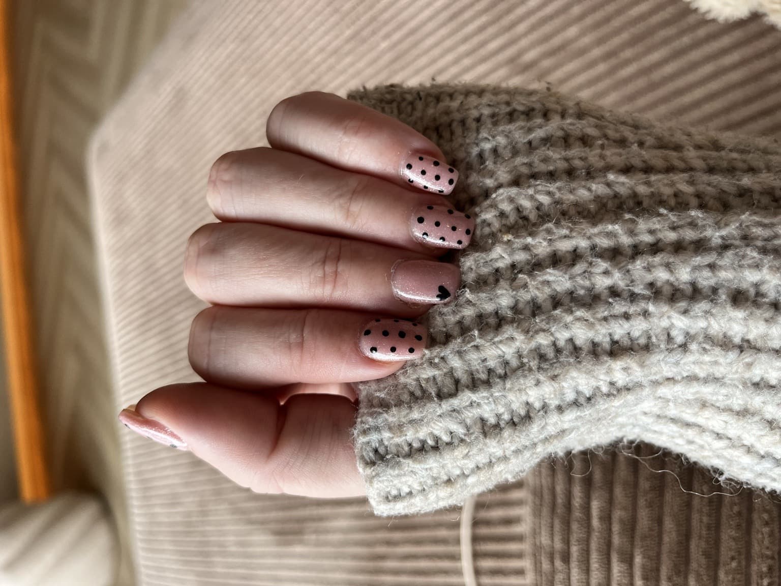 Blush pink short nails with black microdots and a small heart beside a chunky neutral knit sleeve