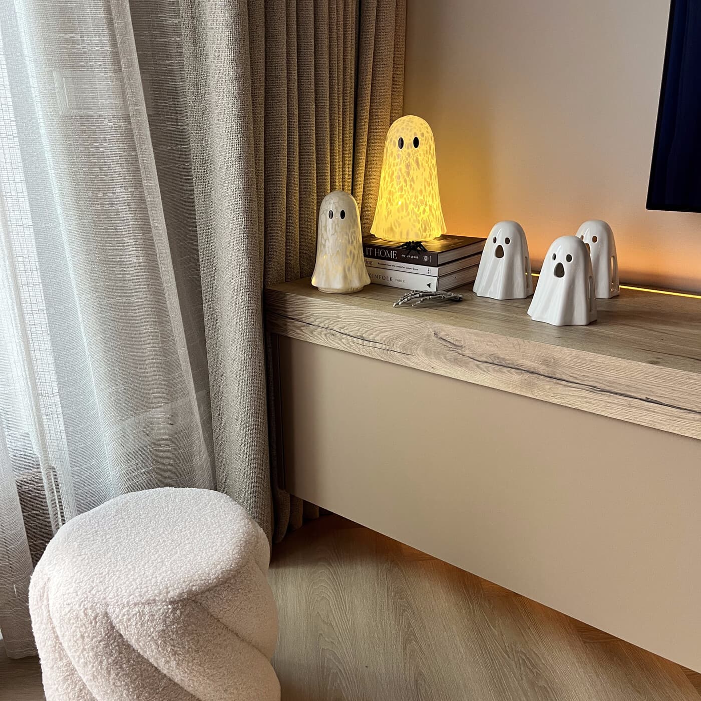A large glowing ghost lamp beside a small stack of books, with four smaller ceramic ghosts on a console table.