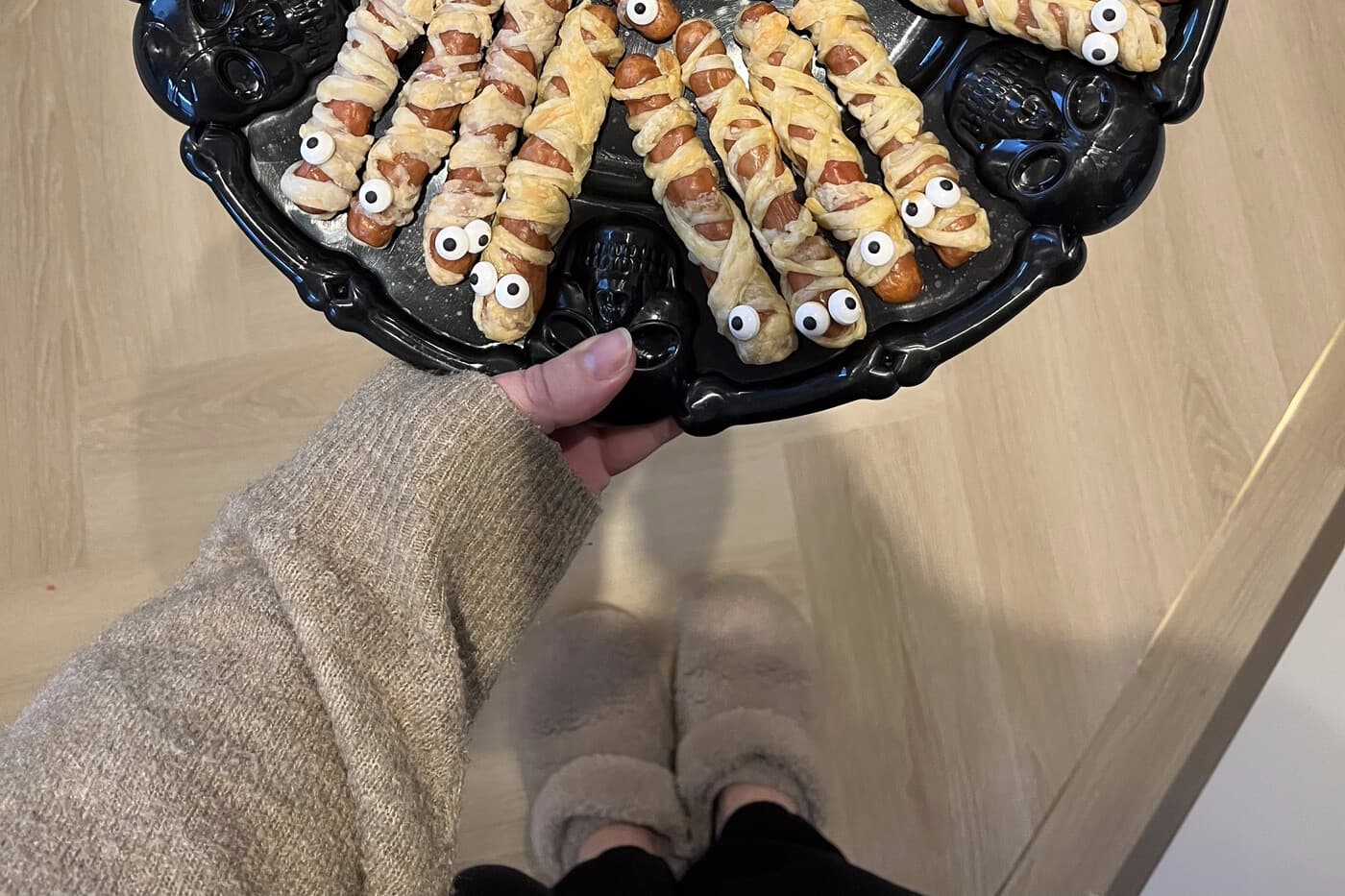 A skull-shaped platter piled with mummy-wrapped sausage rolls, held out for guests.