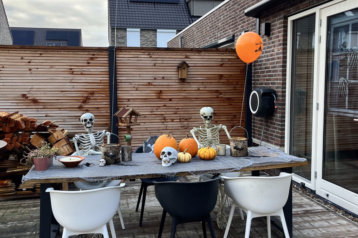 Two seated skeletons at the dressed outdoor table, with carved pumpkins and candles between them.