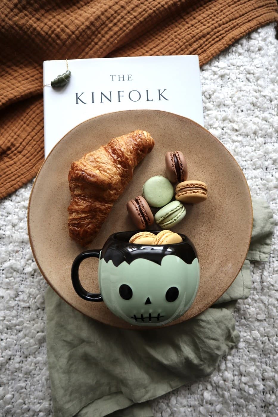 A skull-shaped mug piled with macarons beside a croissant, more macarons and "The Kinfolk" book - cosy, not scary.