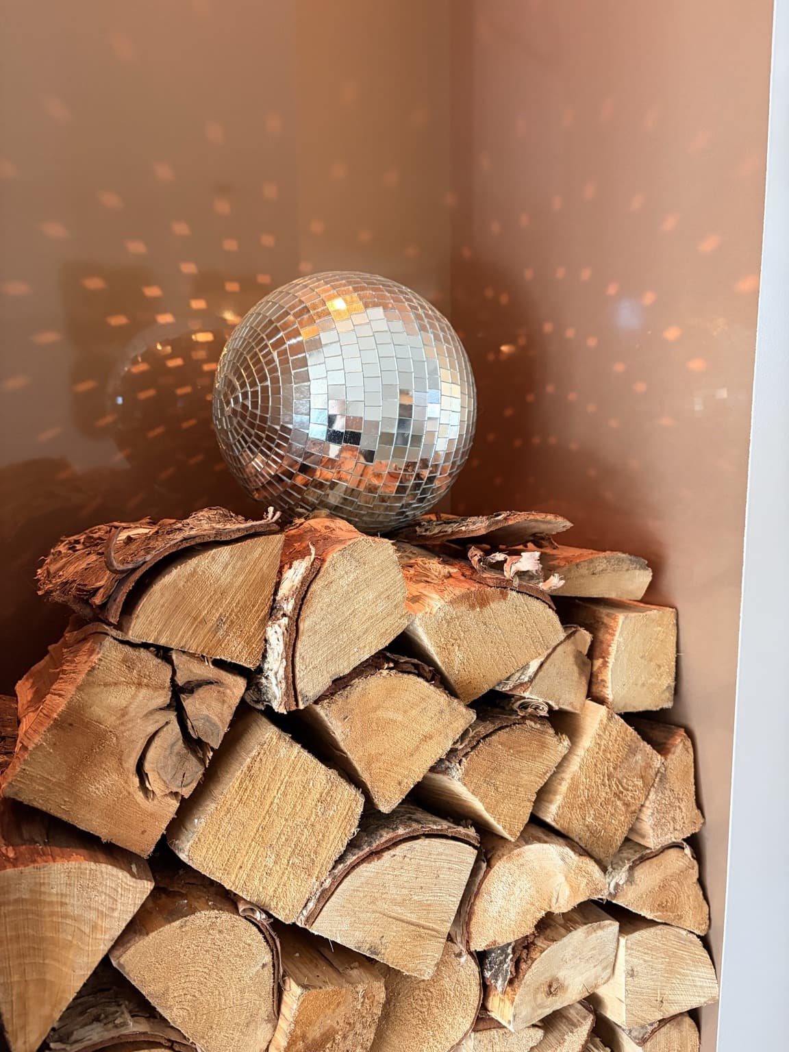 A silver disco ball beside stacked logs in a warm-coloured niche, with reflected spots of light.