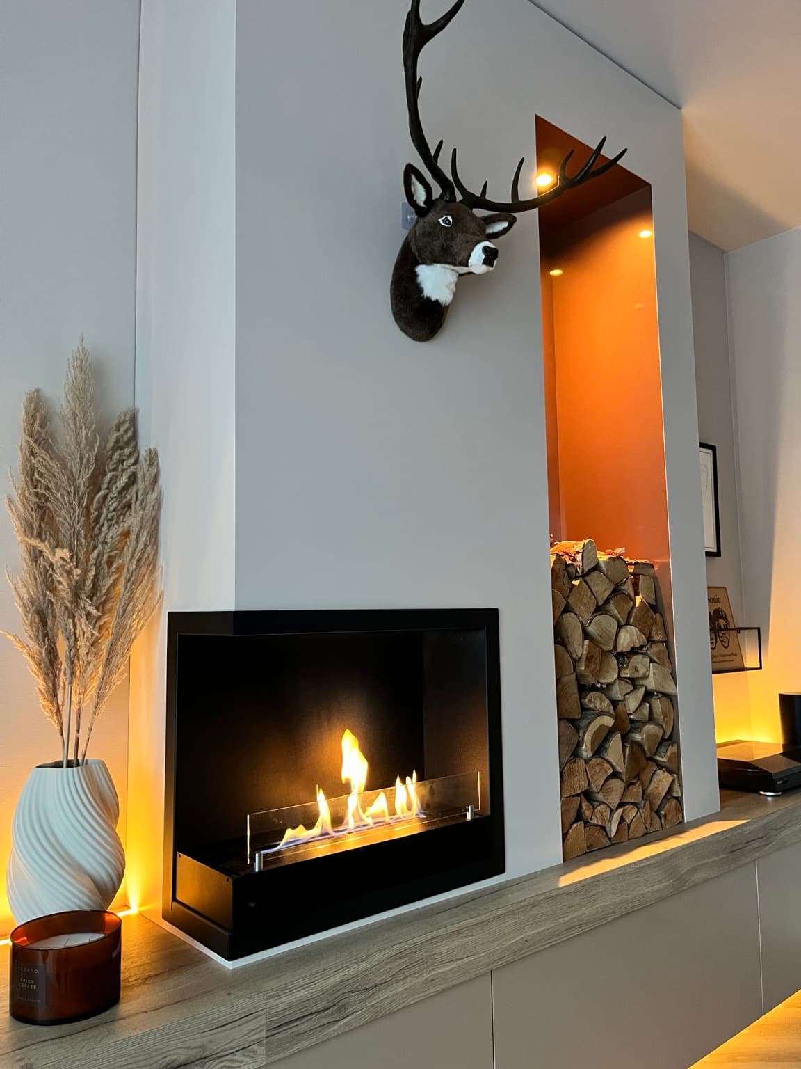 Flames in a black bioethanol fireplace beside a warmly lit alcove with stacked logs.