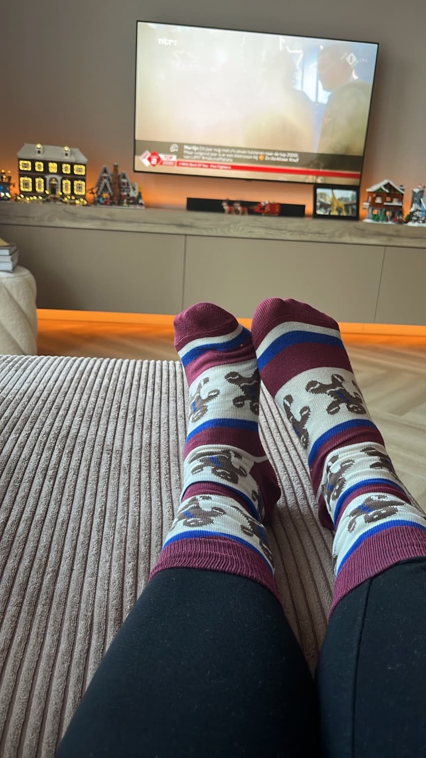Reindeer-patterned socks in the foreground, with a Christmas village along the television cabinet in the background.