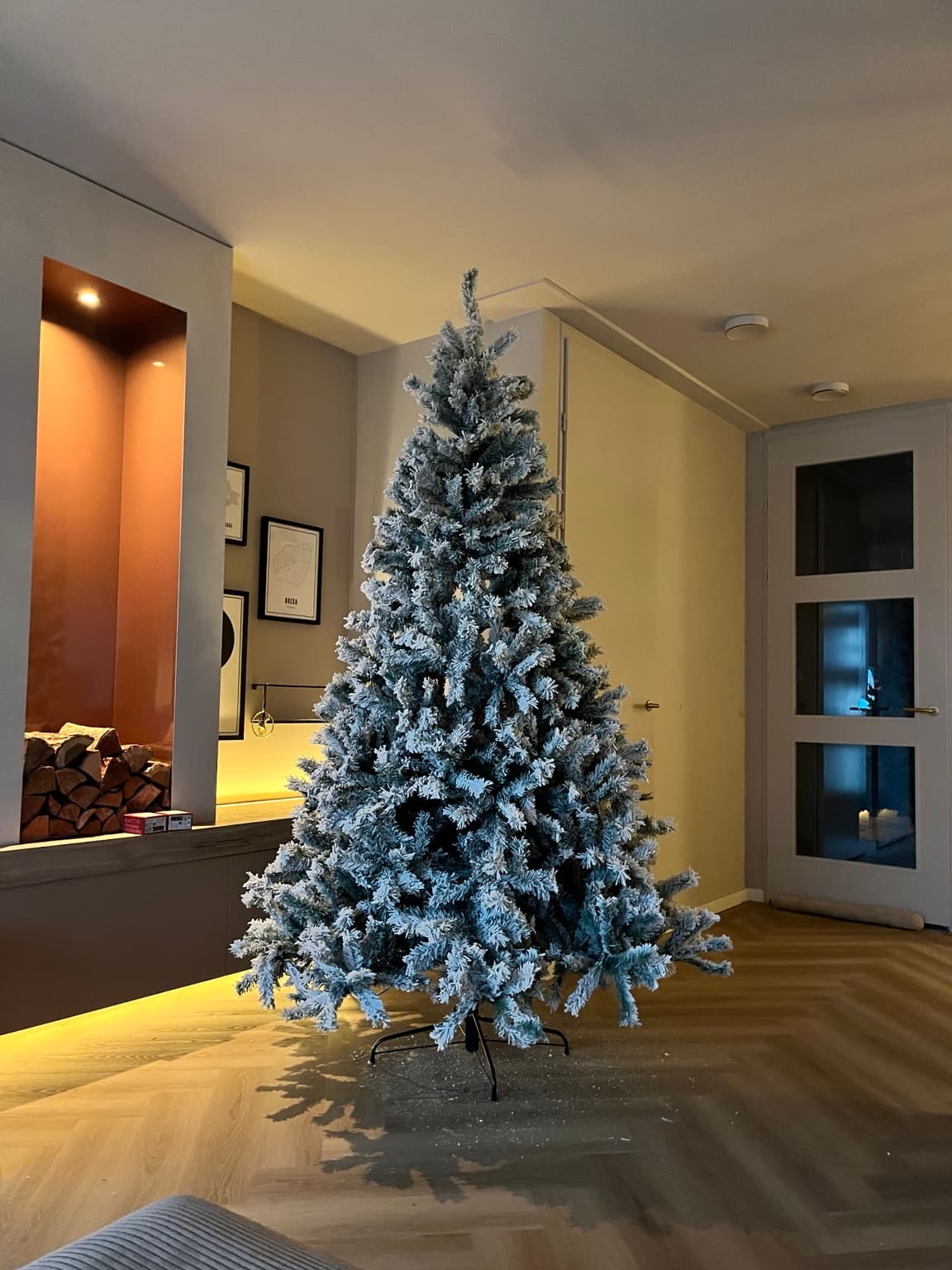 A tall undecorated artificial Christmas tree with snowy branches standing in the living room, before decorating.