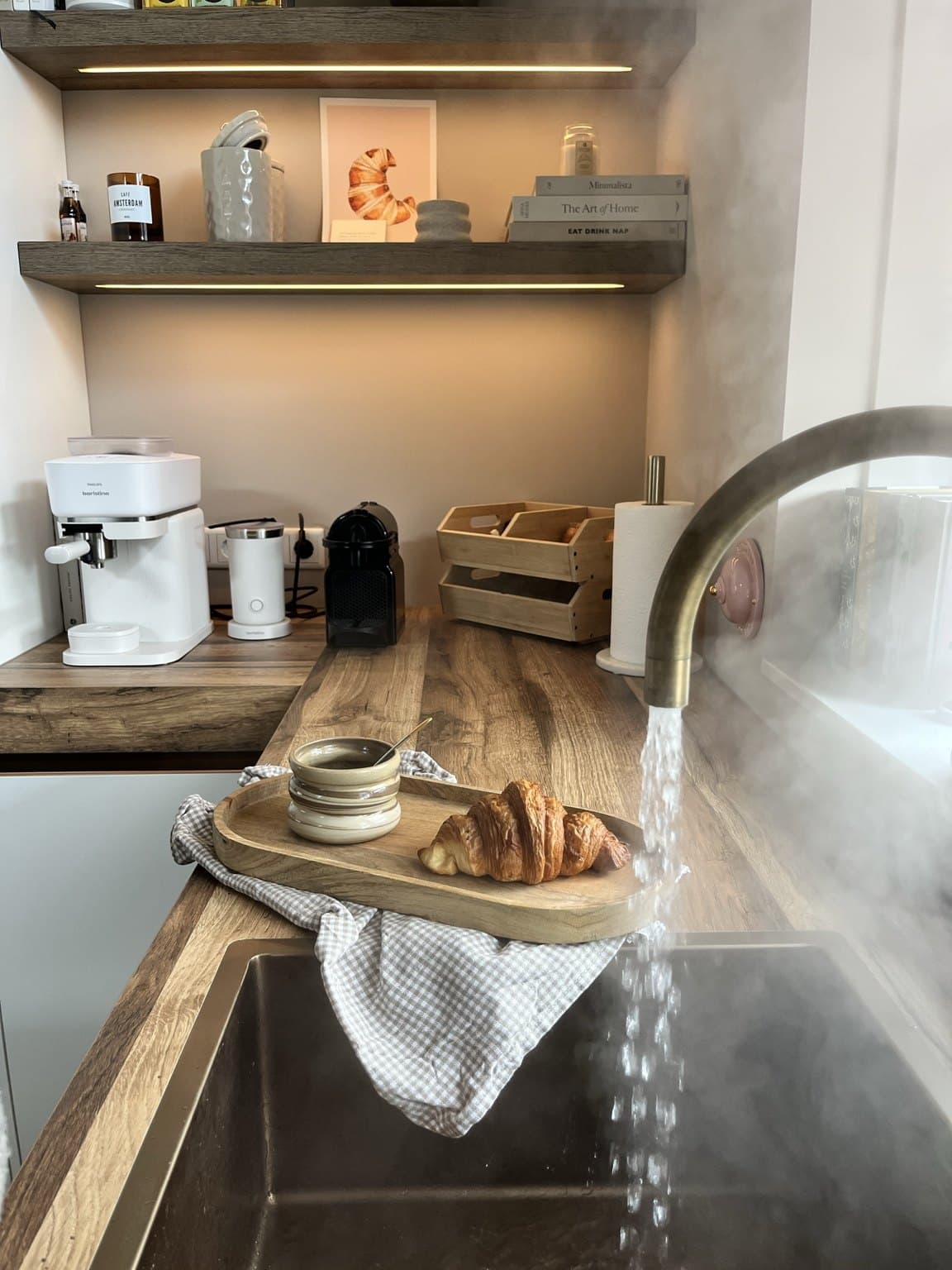 Esther's kitchen coffee corner with illuminated wooden shelves, coffee machines, books and a croissant print.