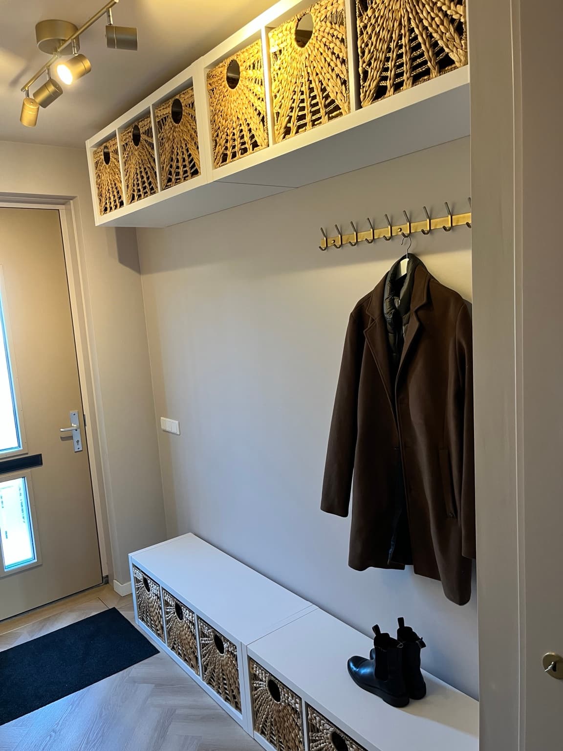 Hallway with woven storage baskets, brass hooks and a bench beneath overhead cupboards.