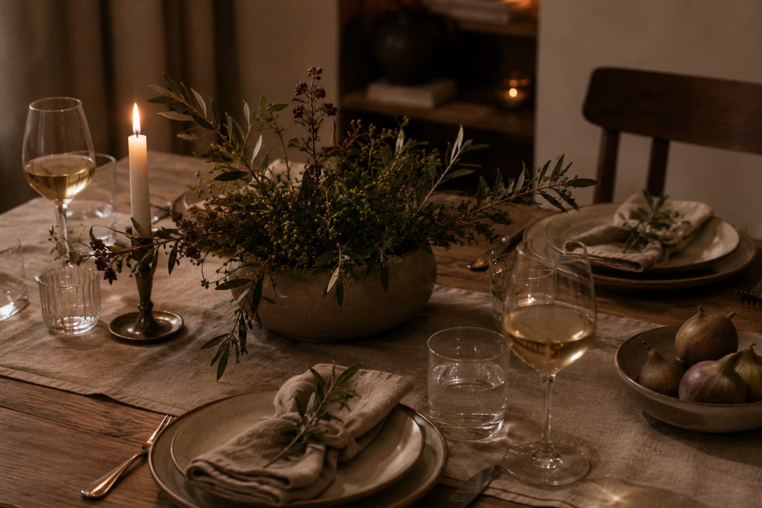 A simple seasonal table setting with one candle, a low centre arrangement and a first drink poured.