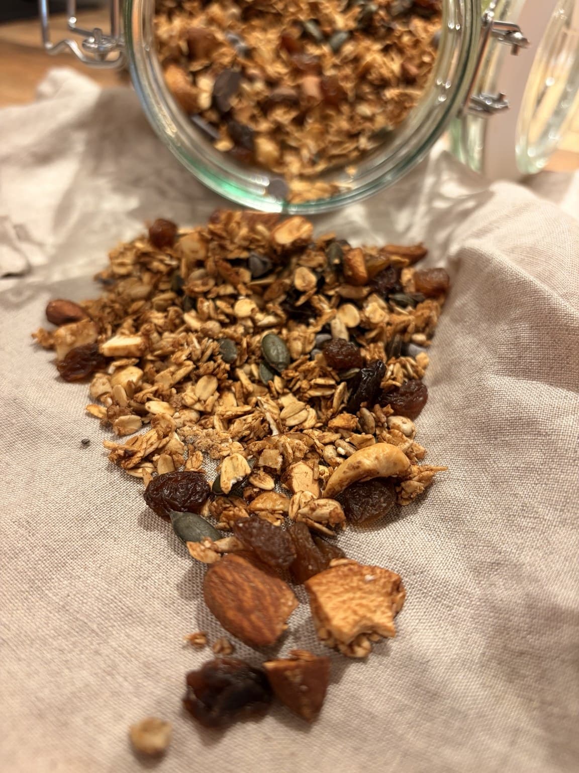 Granola poured out over a linen cloth, showing the texture of oats, nuts and honeyed clusters
