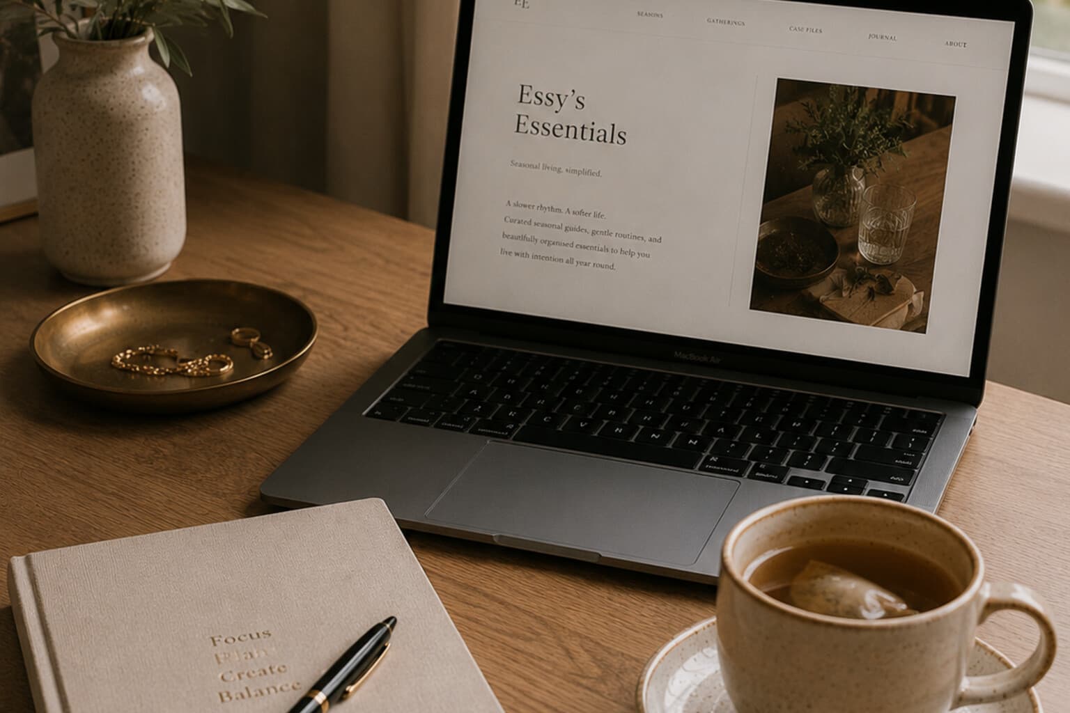 A laptop open on a quiet desk beside a notebook and a cup of tea, soft natural light.