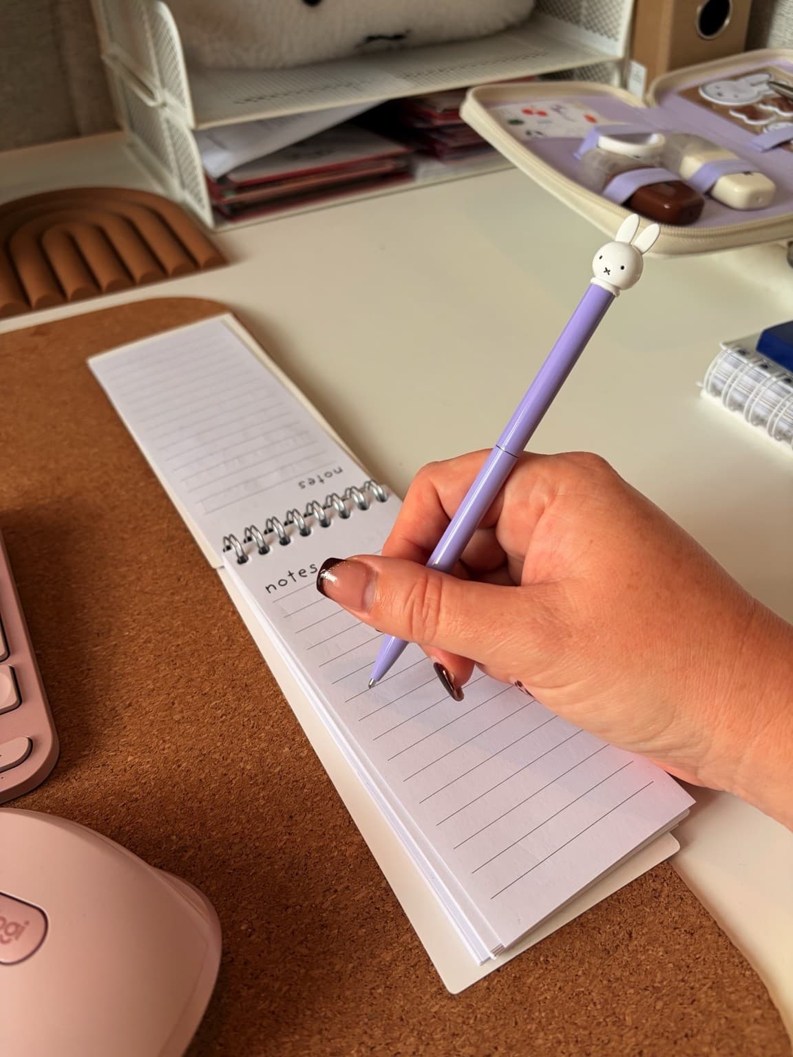 Esther holds a purple Miffy pen over a blank lined notepad on her desk.
