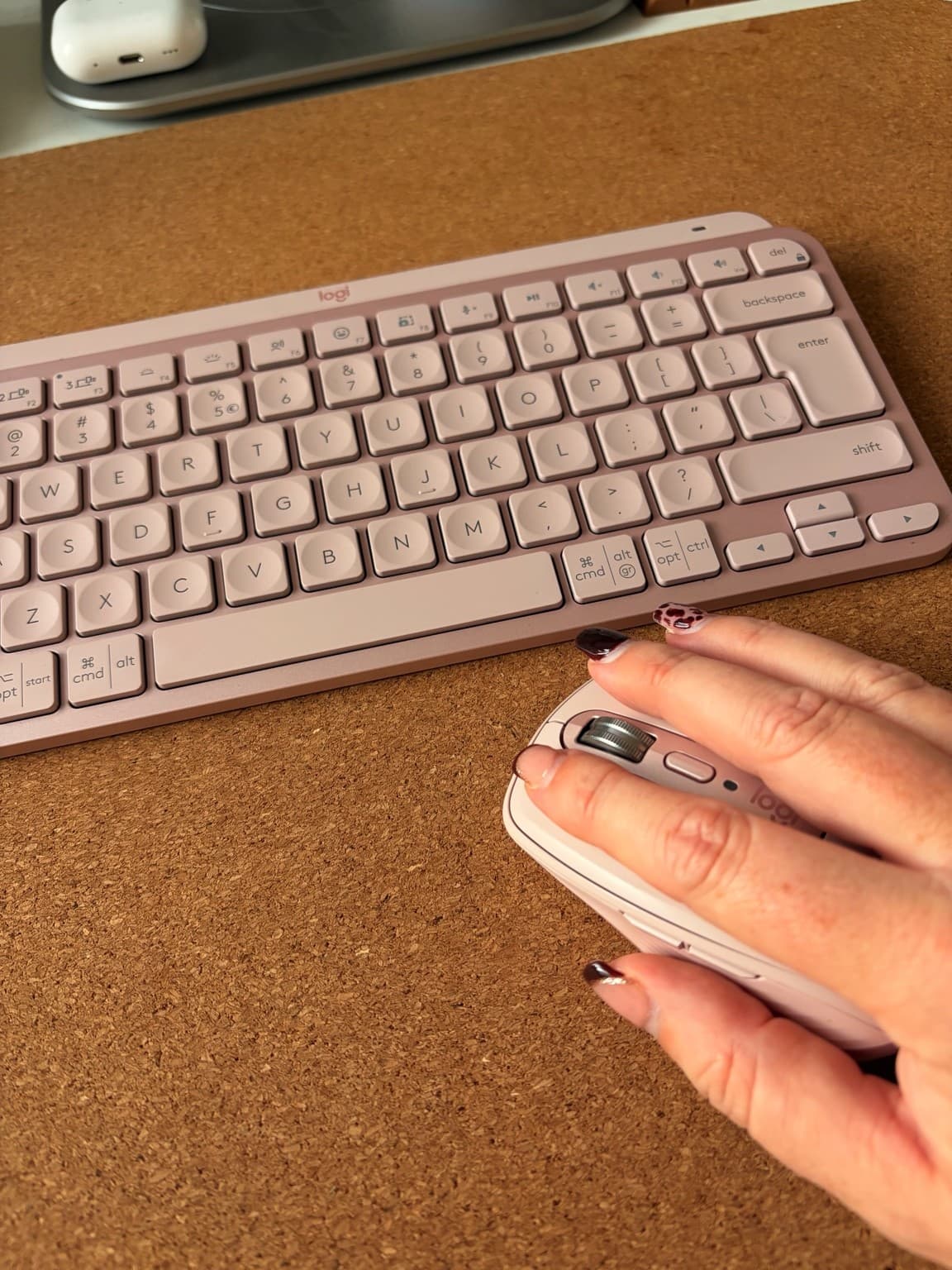 Esther’s hand on a pink mouse beside a matching keyboard on a cork desk mat.