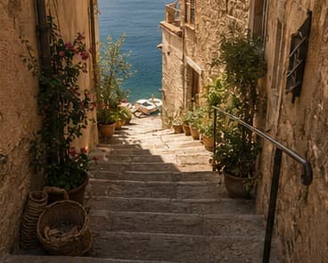 Stone steps in Cortelume descending past sunlit pots toward the harbour at golden hour.
