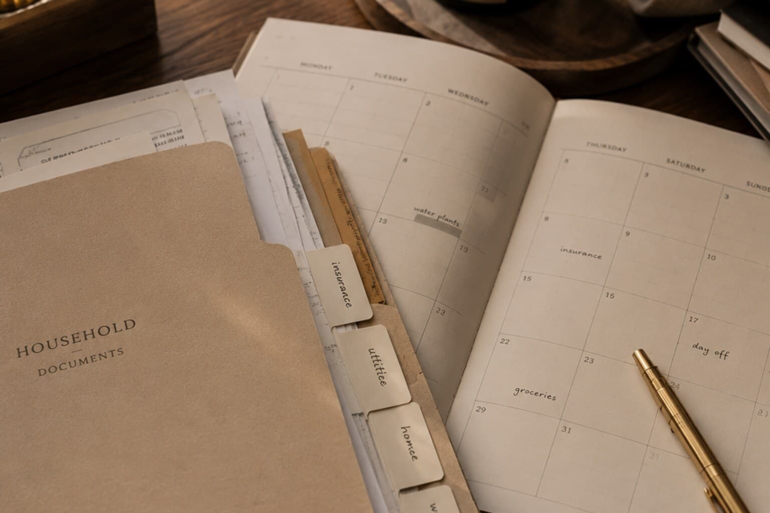 A folder of household documents and a calendar spread open on a table, softly lit.
