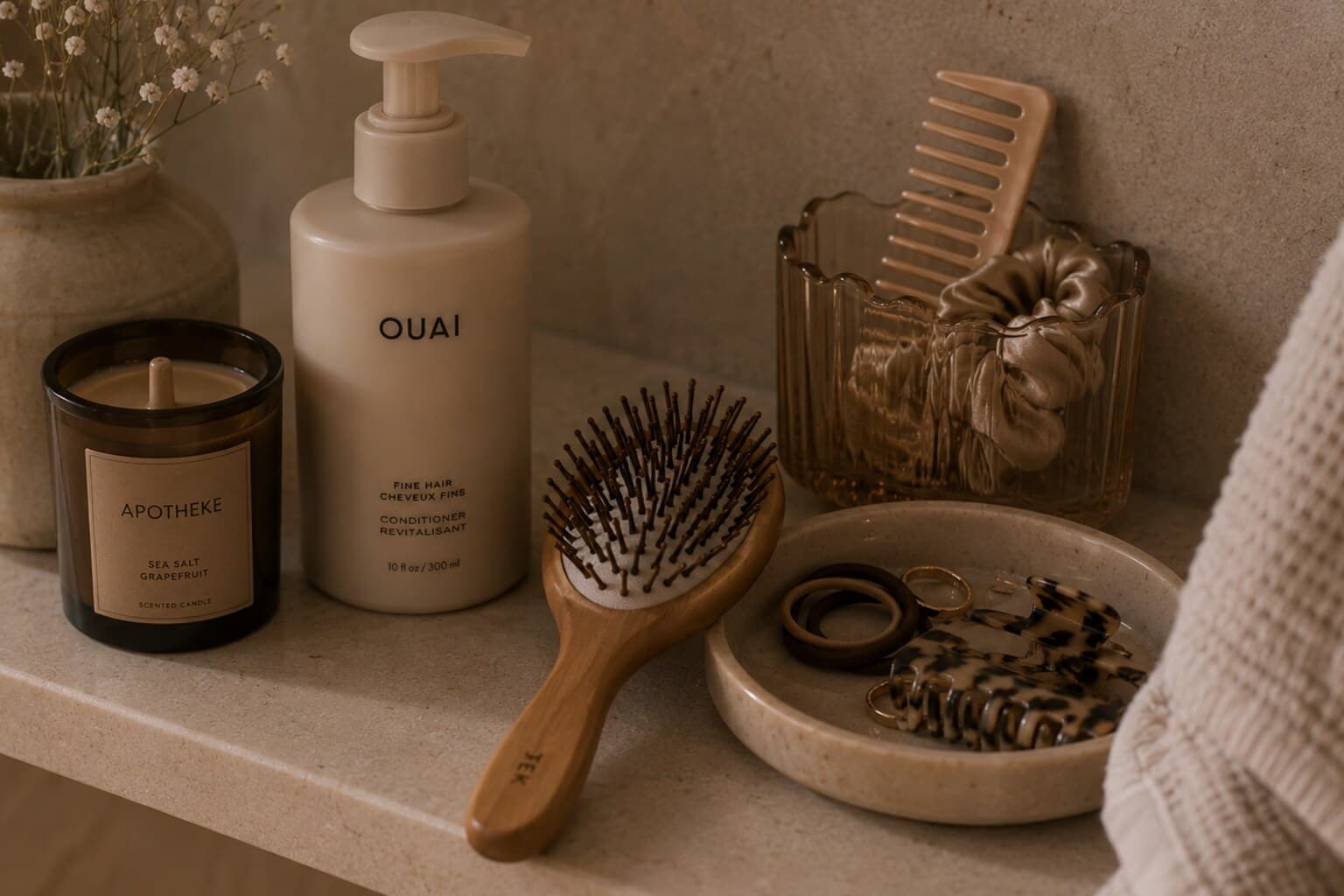 Hair-care tools including a brush, conditioner and hair ties arranged on a bathroom shelf.