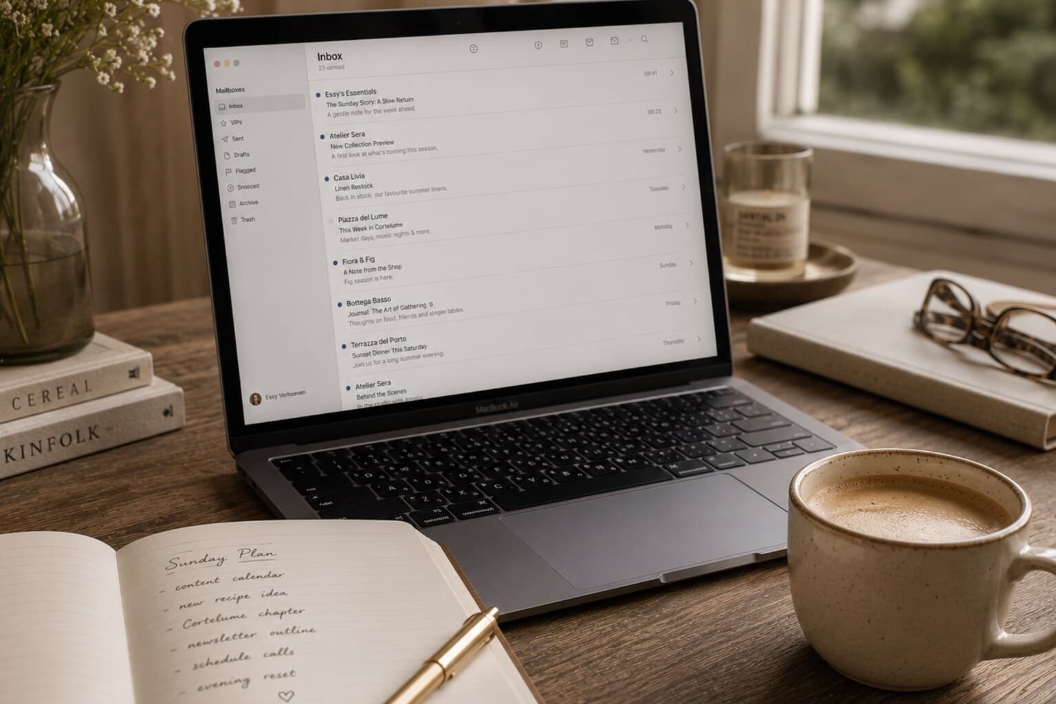 A laptop showing an email inbox beside a notebook and a cup of coffee on a desk.