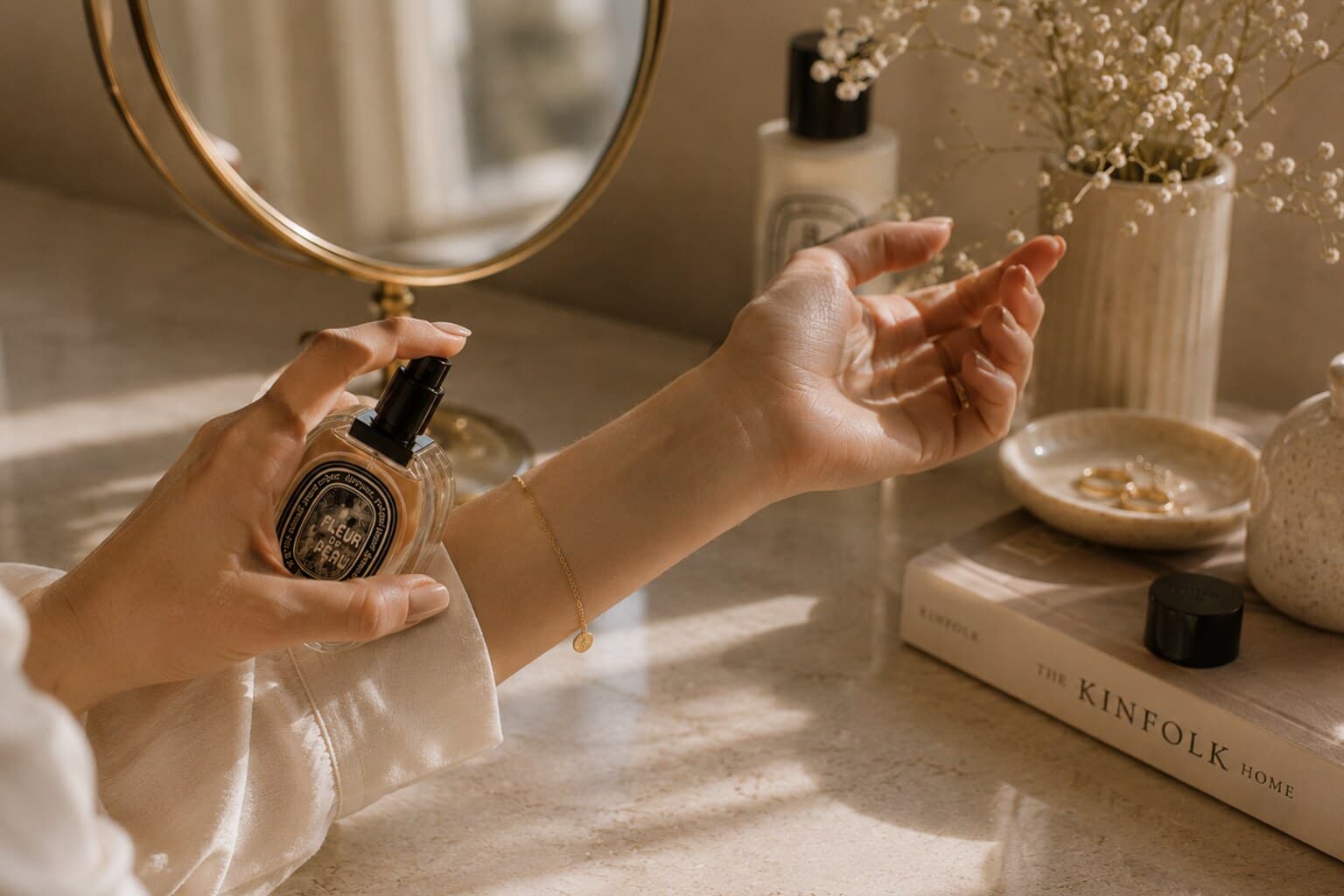 A hand applying perfume to the wrist beside a small mirror in soft morning light.