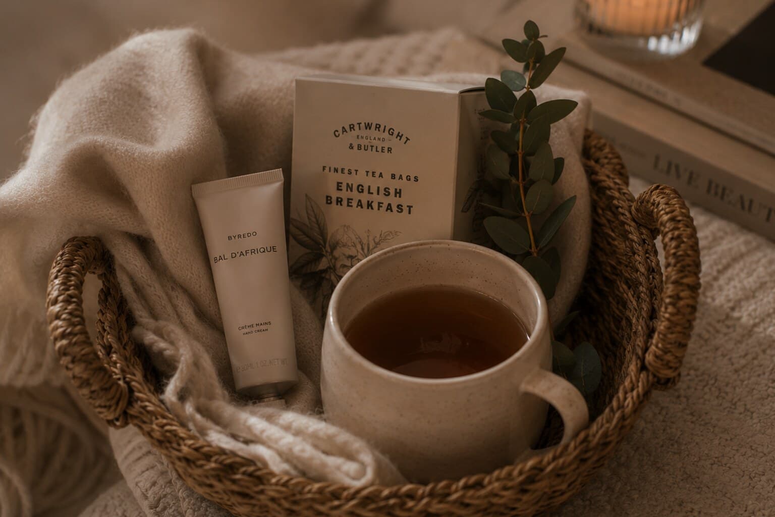 A small woven basket with a blanket, tea and hand cream arranged for a seasonal pause.
