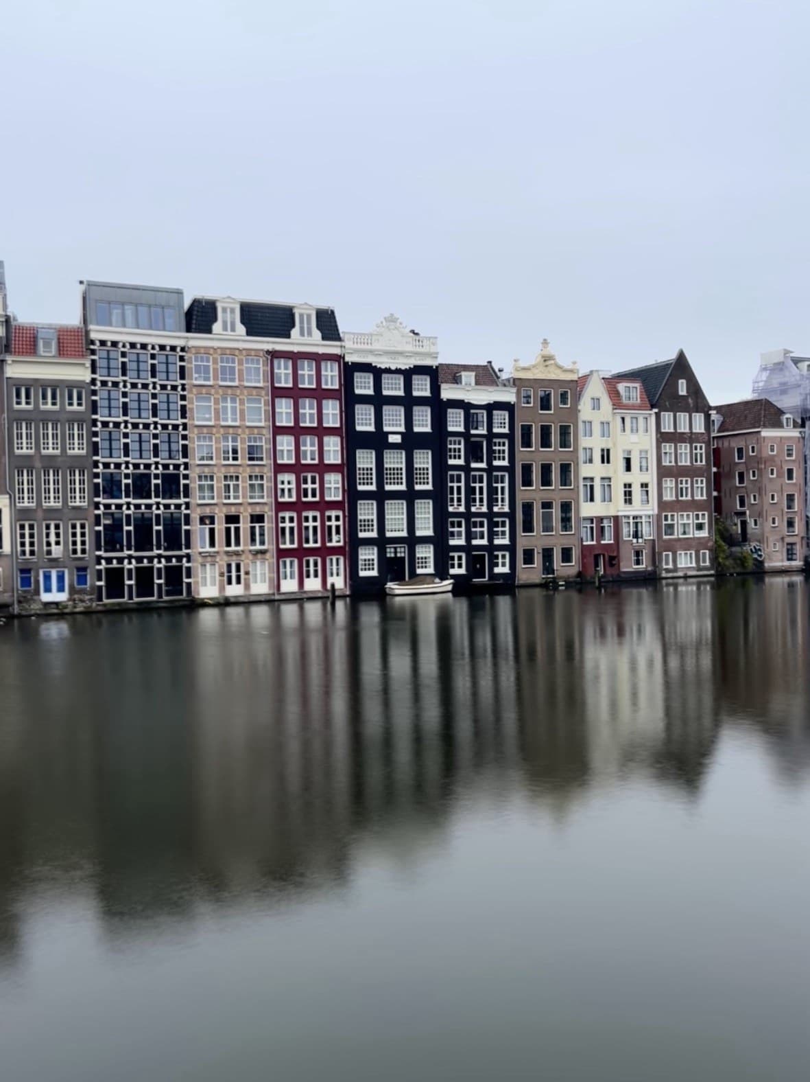 A row of colourful, narrow Amsterdam canal houses reflected in the still water below