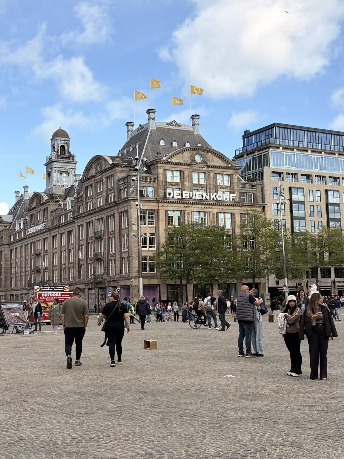 De Bijenkorf department store on Dam Square in Amsterdam, its ornate facade and flags against a blue sky