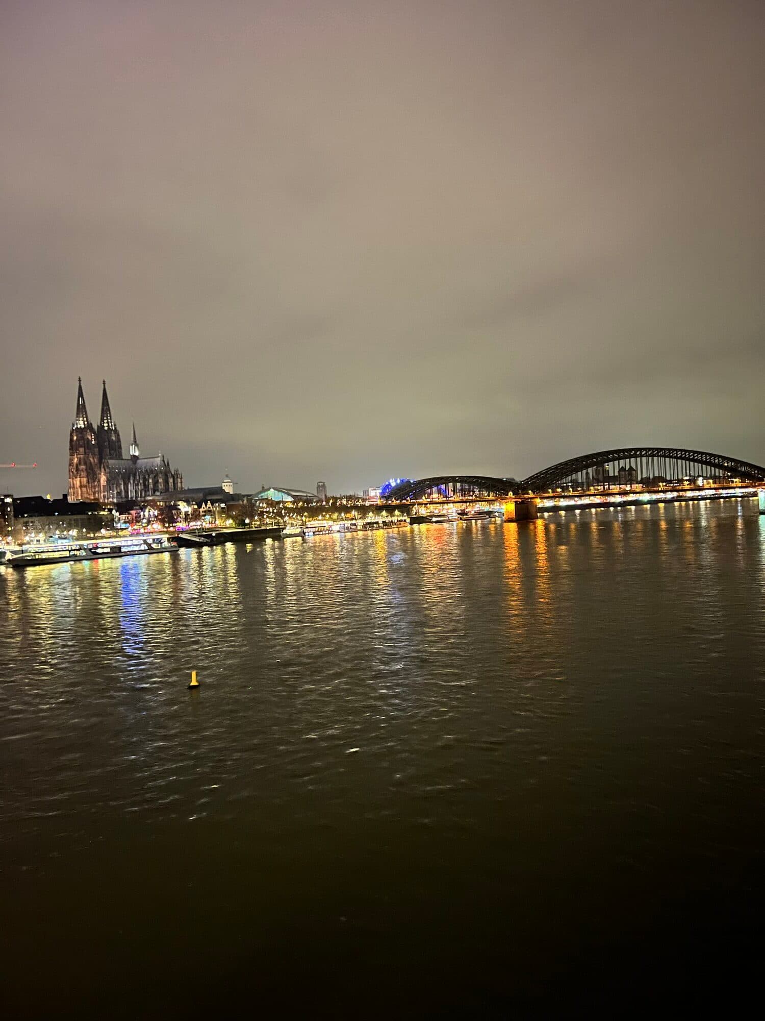 Cologne at night: an illuminated bridge over the Rhine with the Cathedral spires in the distance